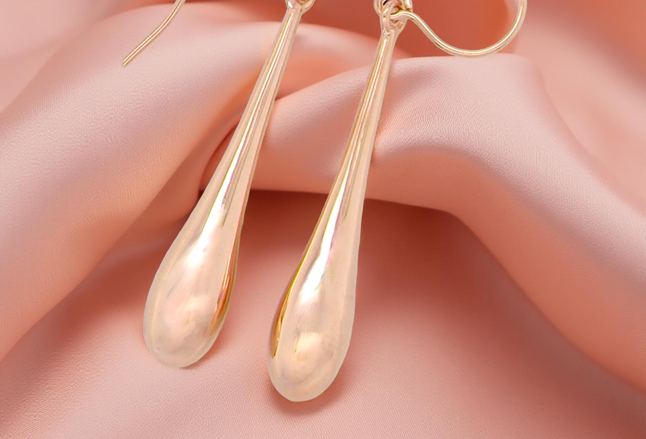 Gold teardrop earrings on a soft pink background