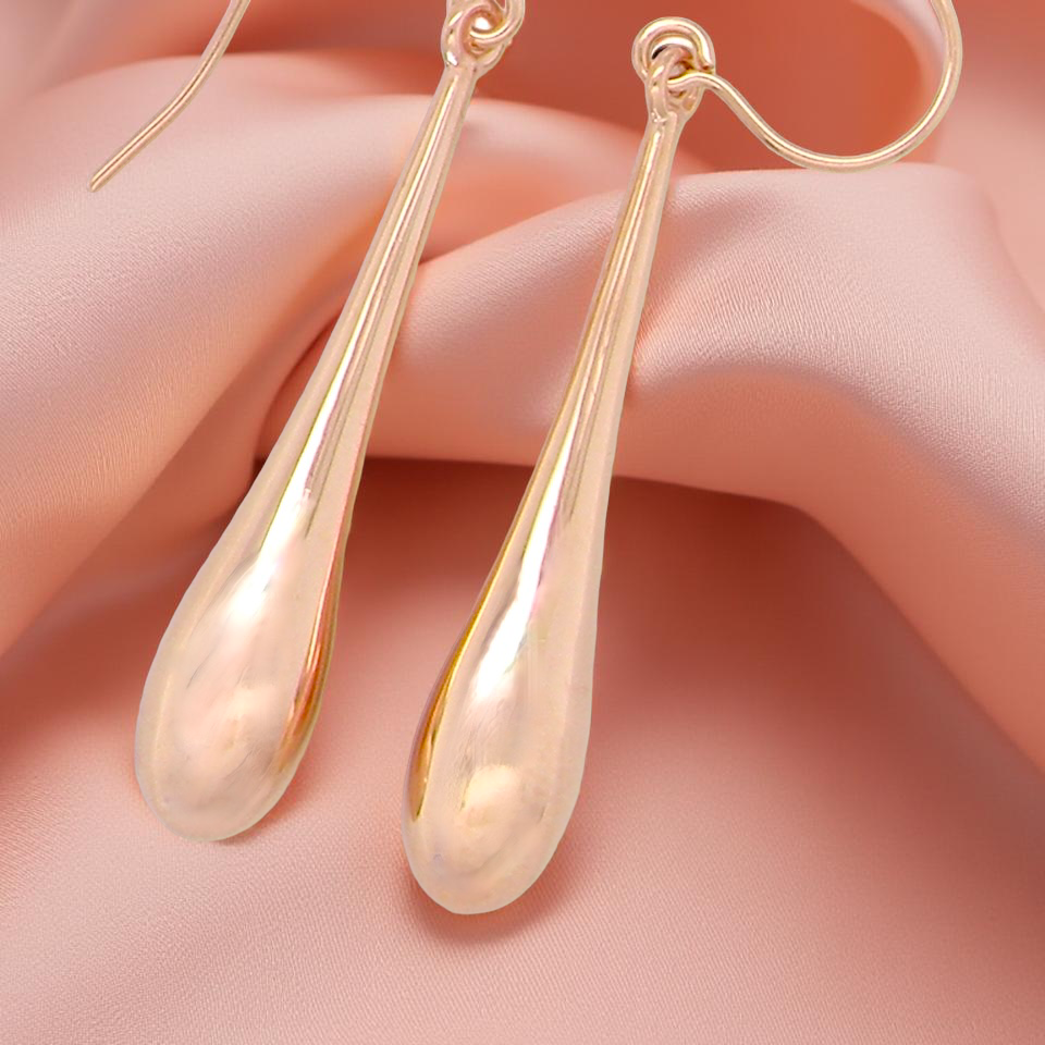 Gold teardrop earrings on a soft pink background
