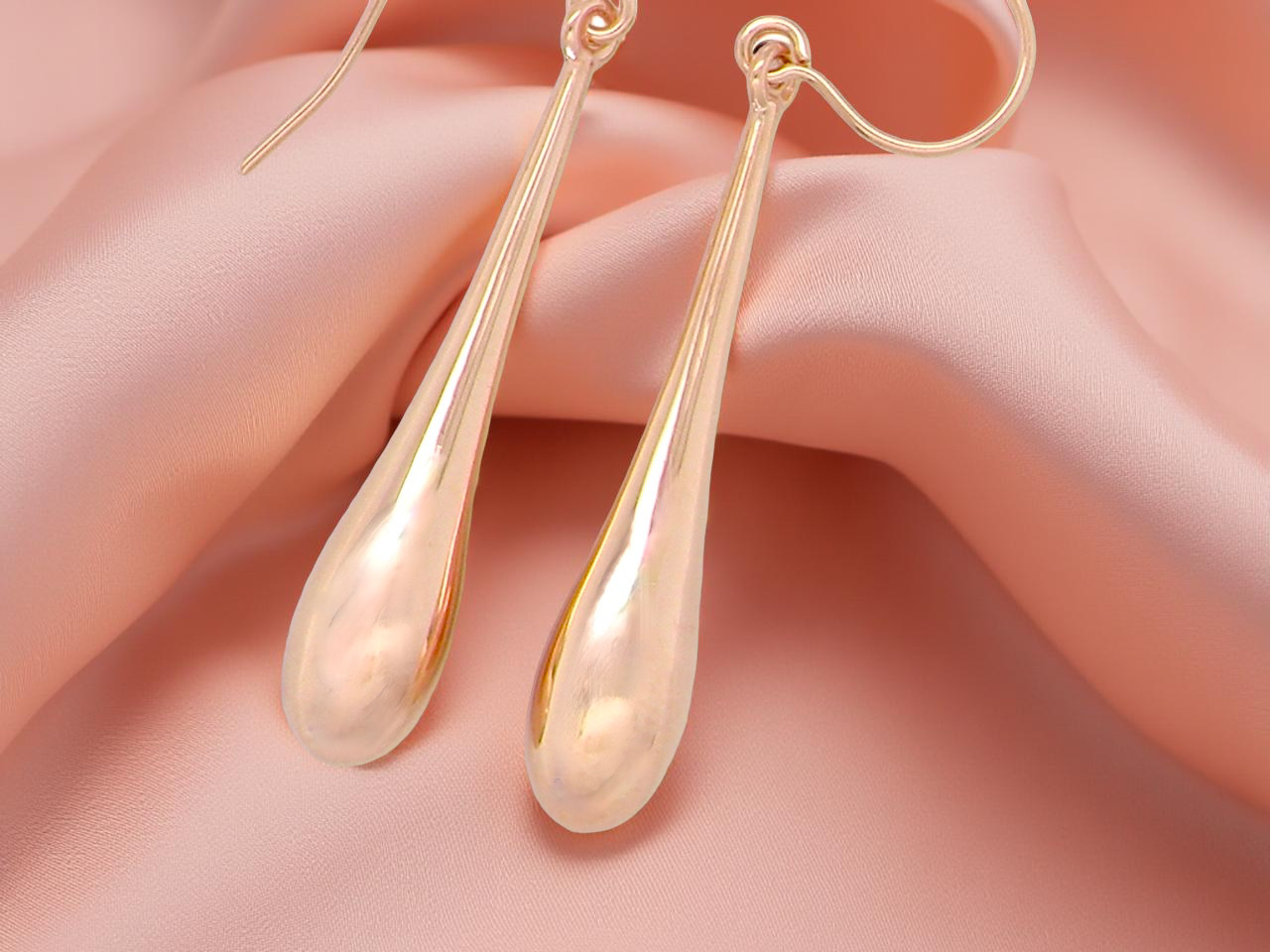 Gold teardrop earrings on a soft pink background