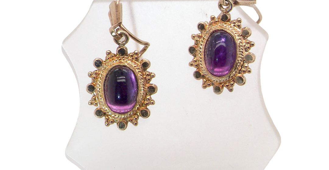 A pair of drop earrings. Each set with a cabouchon cut amethyst 6x4mm and set with an antique look border.