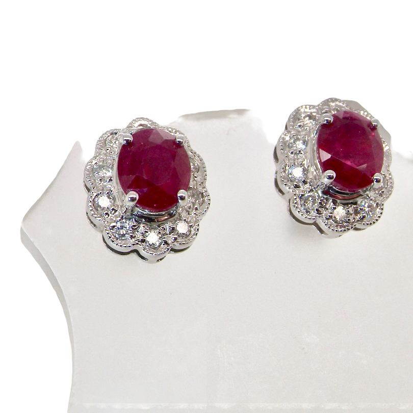 A pair of white gold earrings, each set with an oval ruby 6x4.9mm (est 0.60 carats) complimented by an outer halo of ten diamonds