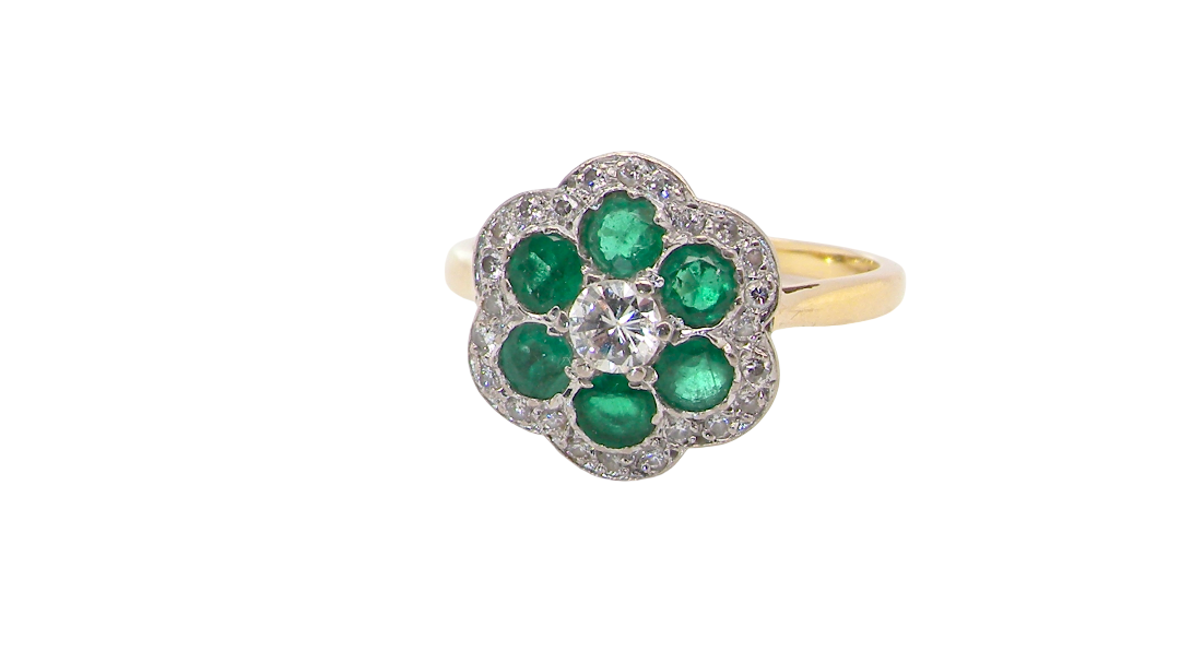 A pretty cluster ring. Features emeralds and diamonds. Centre stone a brilliant cut white diamond, measures 4mm