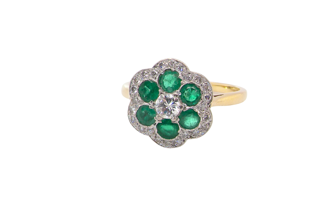 A pretty cluster ring. Features emeralds and diamonds. Centre stone a brilliant cut white diamond, measures 4mm