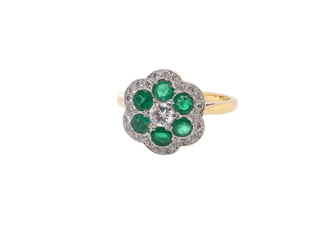 A pretty cluster ring. Features emeralds and diamonds. Centre stone a brilliant cut white diamond, measures 4mm