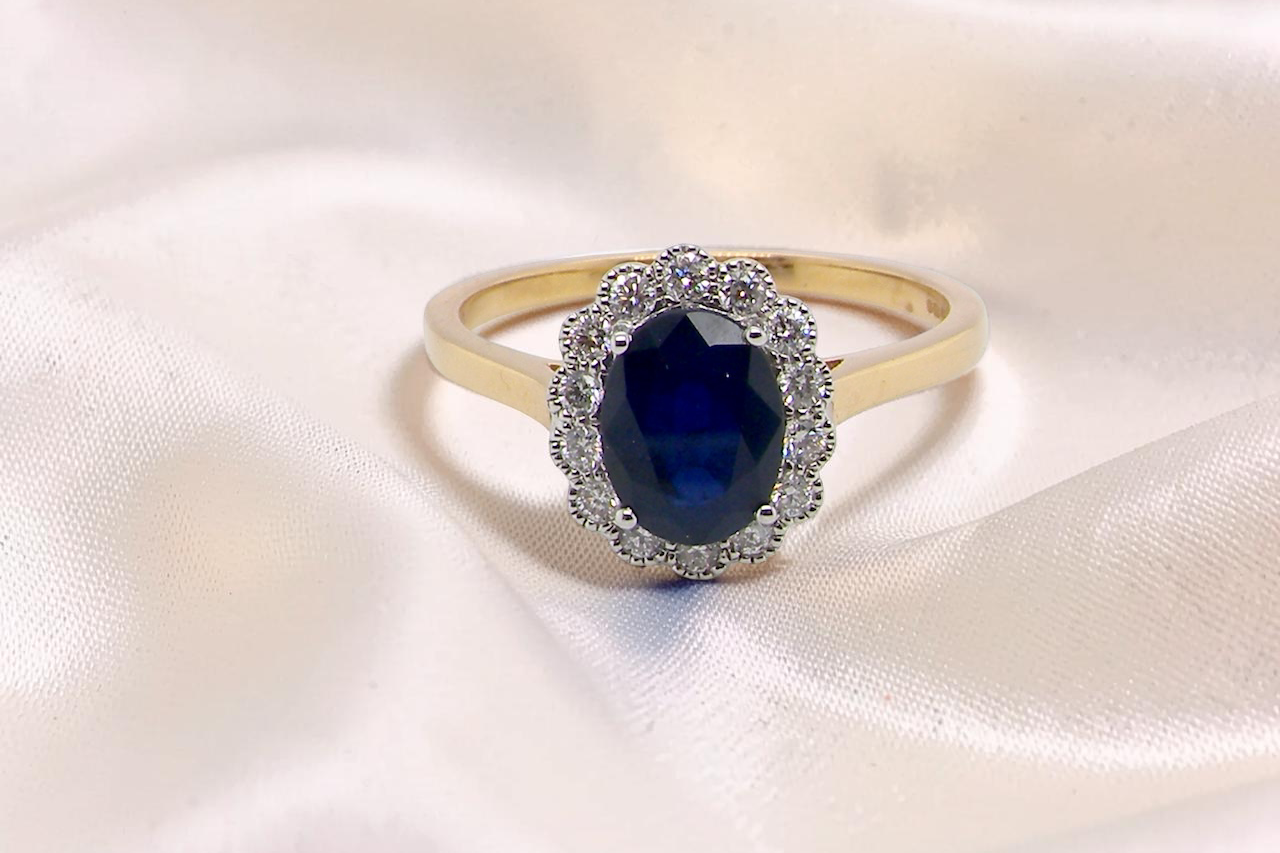 A pretty cluster ring that features an inky black blue sapphire that measures 8x6mm. Complimented by an outer border of diamonds