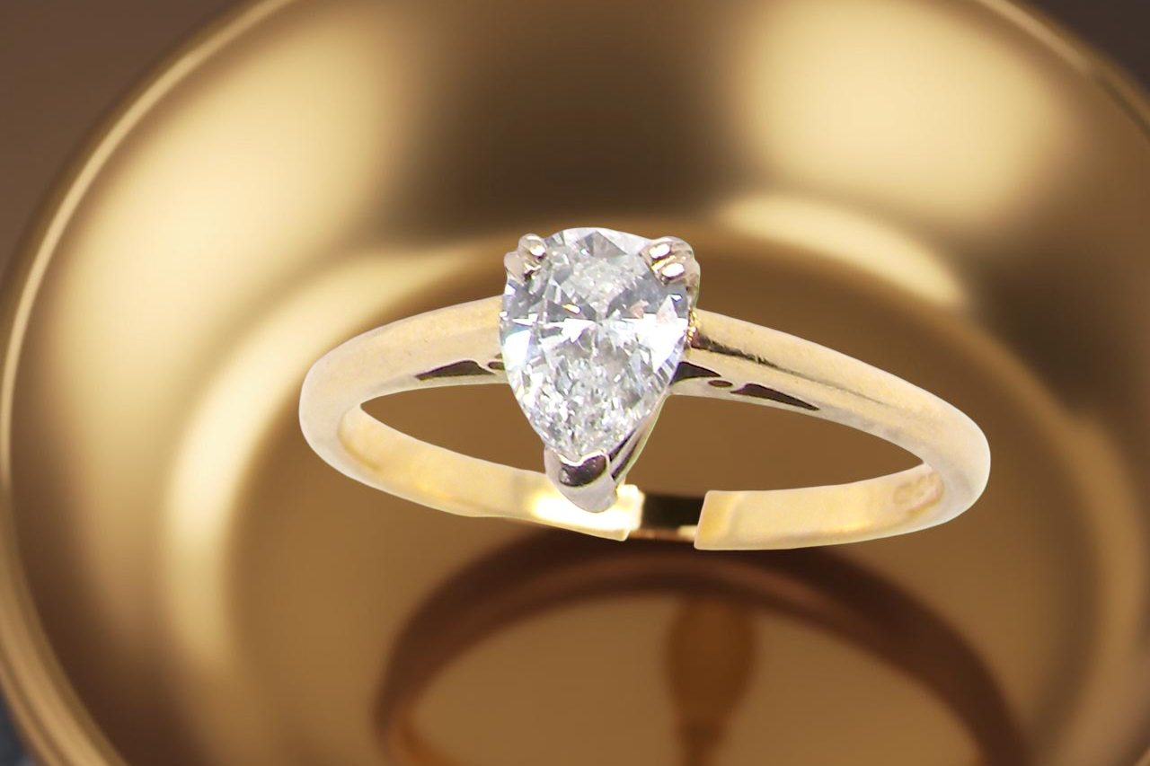 Gold ring with a pear-shaped diamond on a reflective gold surface