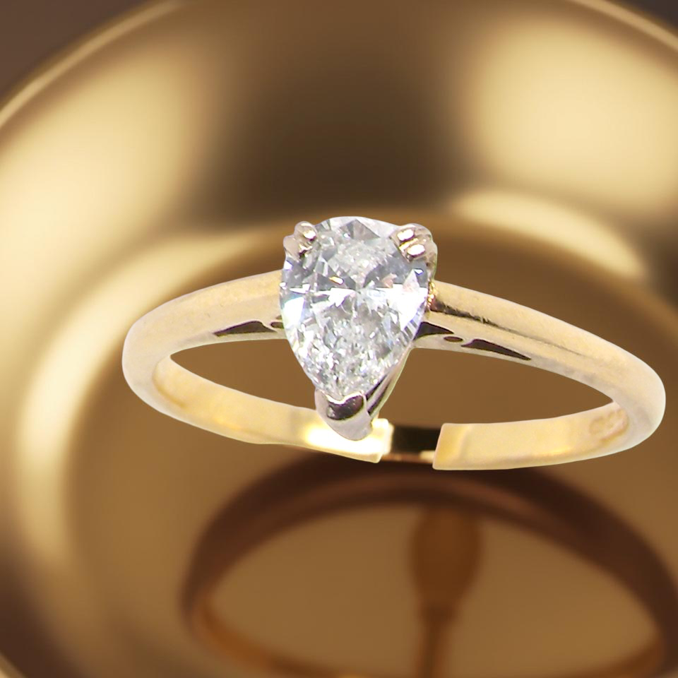 Gold ring with a pear-shaped diamond on a reflective gold surface