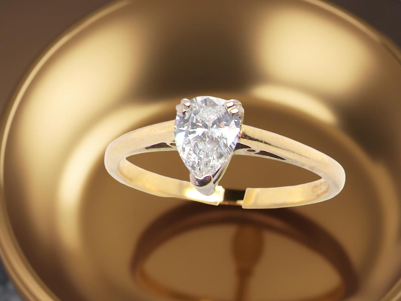 Gold ring with a pear-shaped diamond on a reflective gold surface