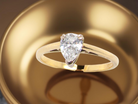 Gold ring with a pear-shaped diamond on a reflective gold surface