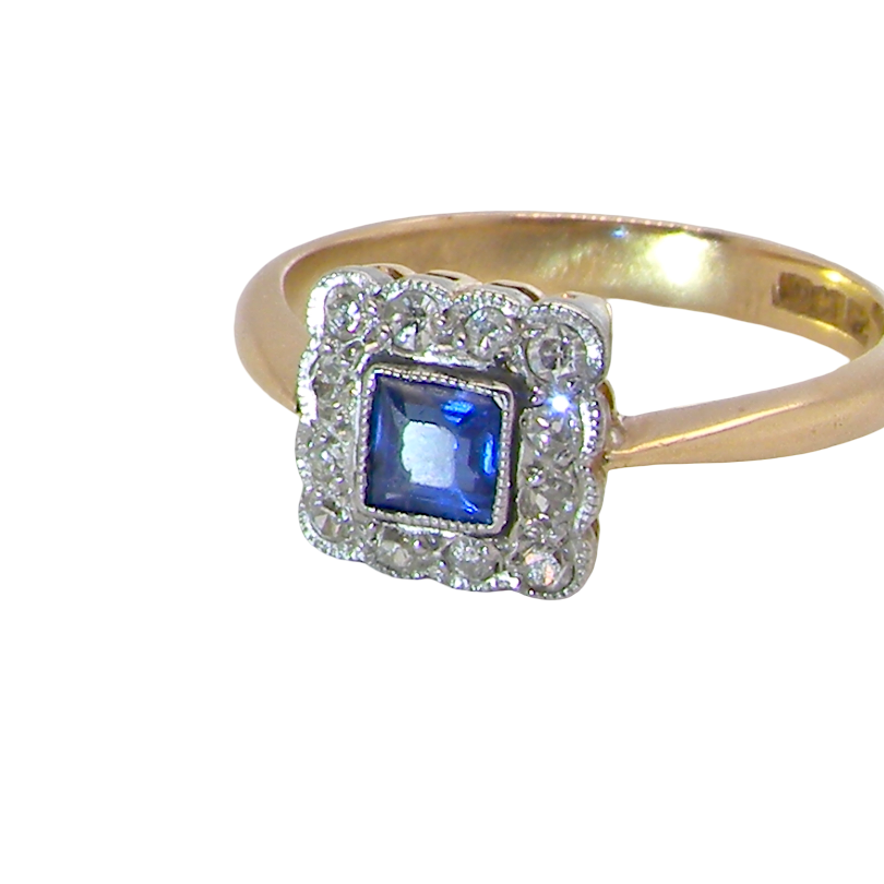 A pretty square cluster ring. Features to the centre a cornflower blue square sapphire, 4x4mm (est 0.30 carats) mille grain set.
Complimented by a halo of twelve single cut white diamonds