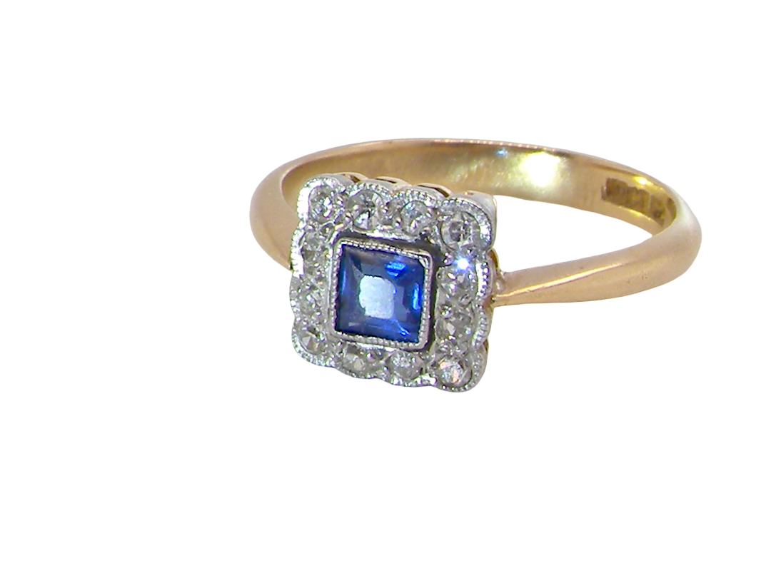 A pretty square cluster ring. Features to the centre a cornflower blue square sapphire, 4x4mm (est 0.30 carats) mille grain set.
Complimented by a halo of twelve single cut white diamonds