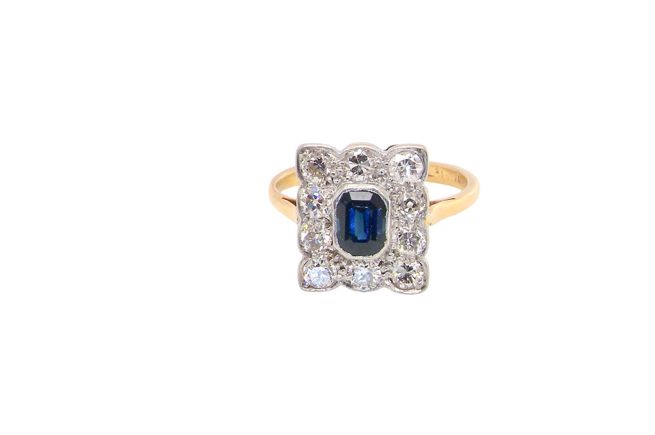 A rectangular cluster ring that features in its centre a cushion shaped dark blue sapphire, that measures 5x3.5mm (est 0.30 carats)