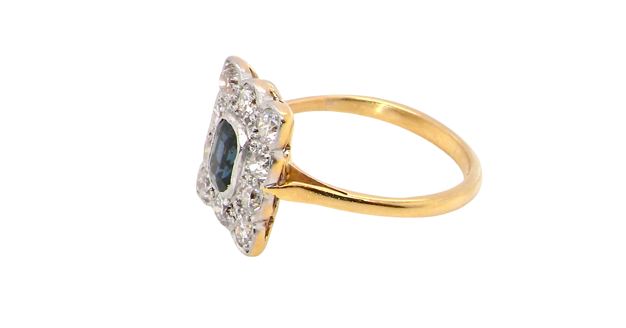 A rectangular cluster ring that features in its centre a cushion shaped dark blue sapphire, that measures 5x3.5mm (est 0.30 carats) side