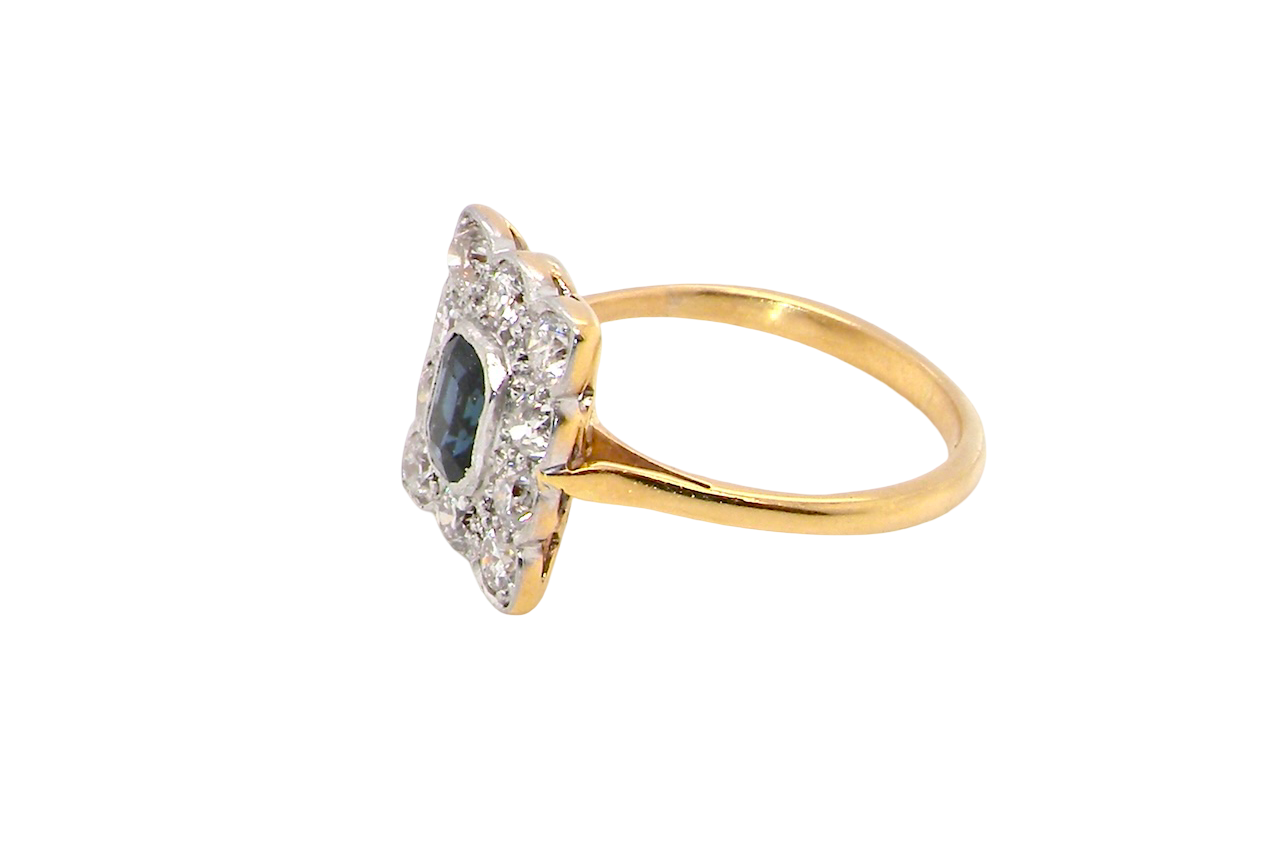 A rectangular cluster ring that features in its centre a cushion shaped dark blue sapphire, that measures 5x3.5mm (est 0.30 carats) side