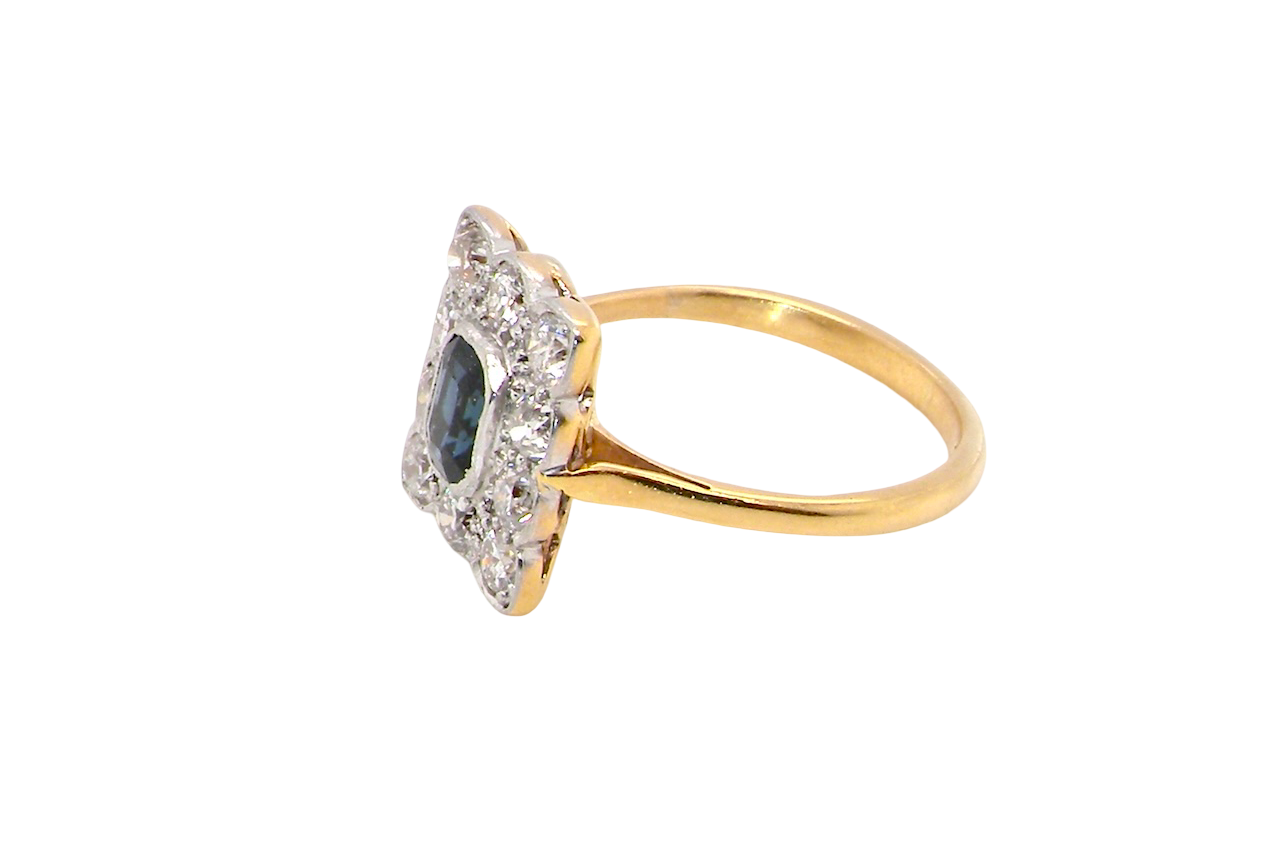 A rectangular cluster ring that features in its centre a cushion shaped dark blue sapphire, that measures 5x3.5mm (est 0.30 carats) side