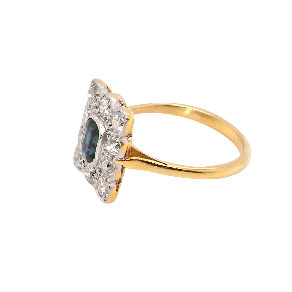 A rectangular cluster ring that features in its centre a cushion shaped dark blue sapphire, that measures 5x3.5mm (est 0.30 carats) side