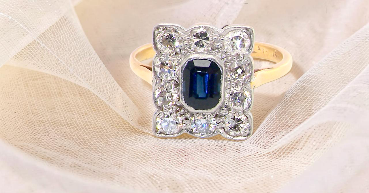 A rectangular cluster ring that features in its centre a cushion shaped dark blue sapphire, that measures (est 0.30 carats)