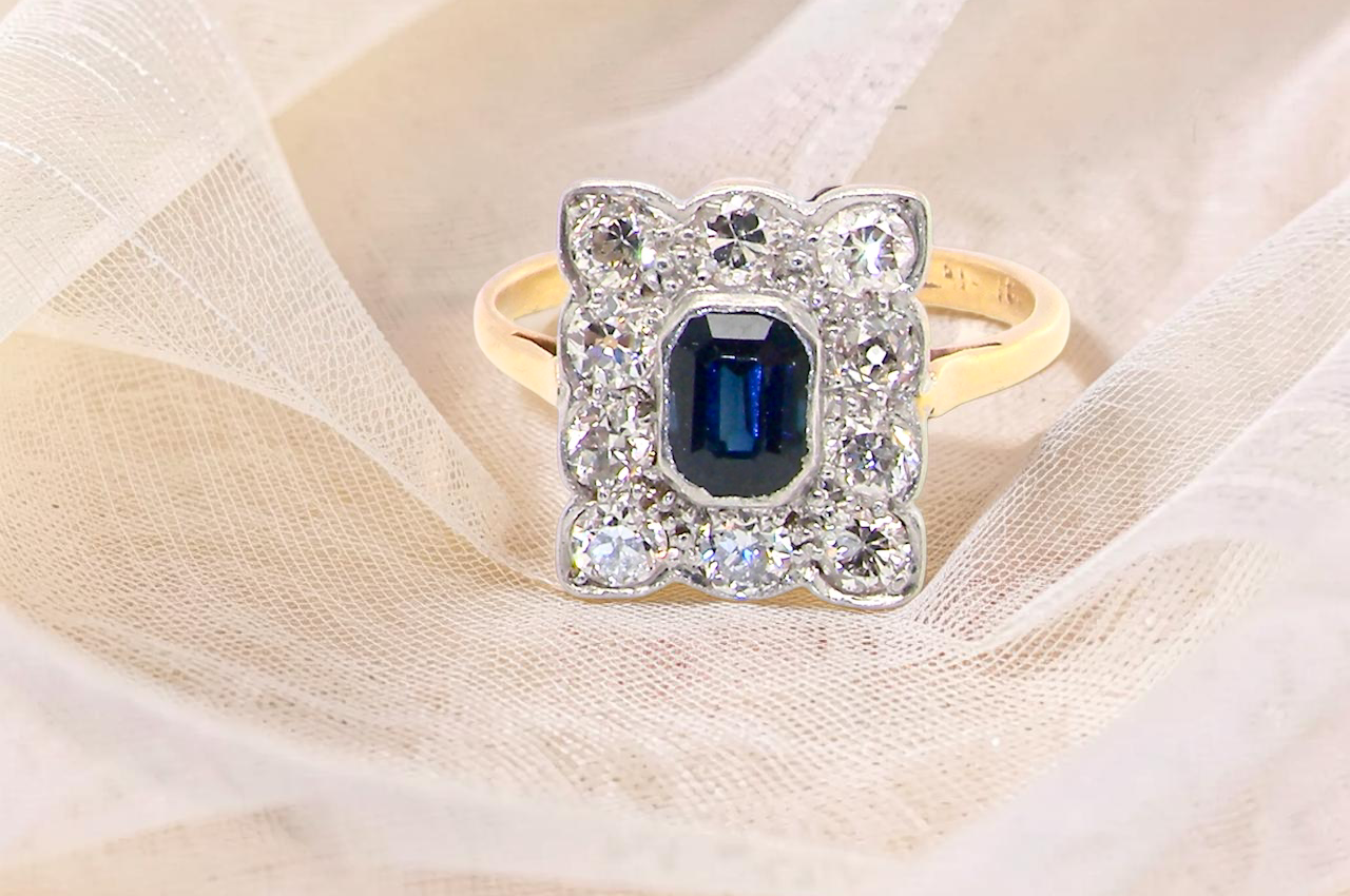 A rectangular cluster ring that features in its centre a cushion shaped dark blue sapphire, that measures (est 0.30 carats)
