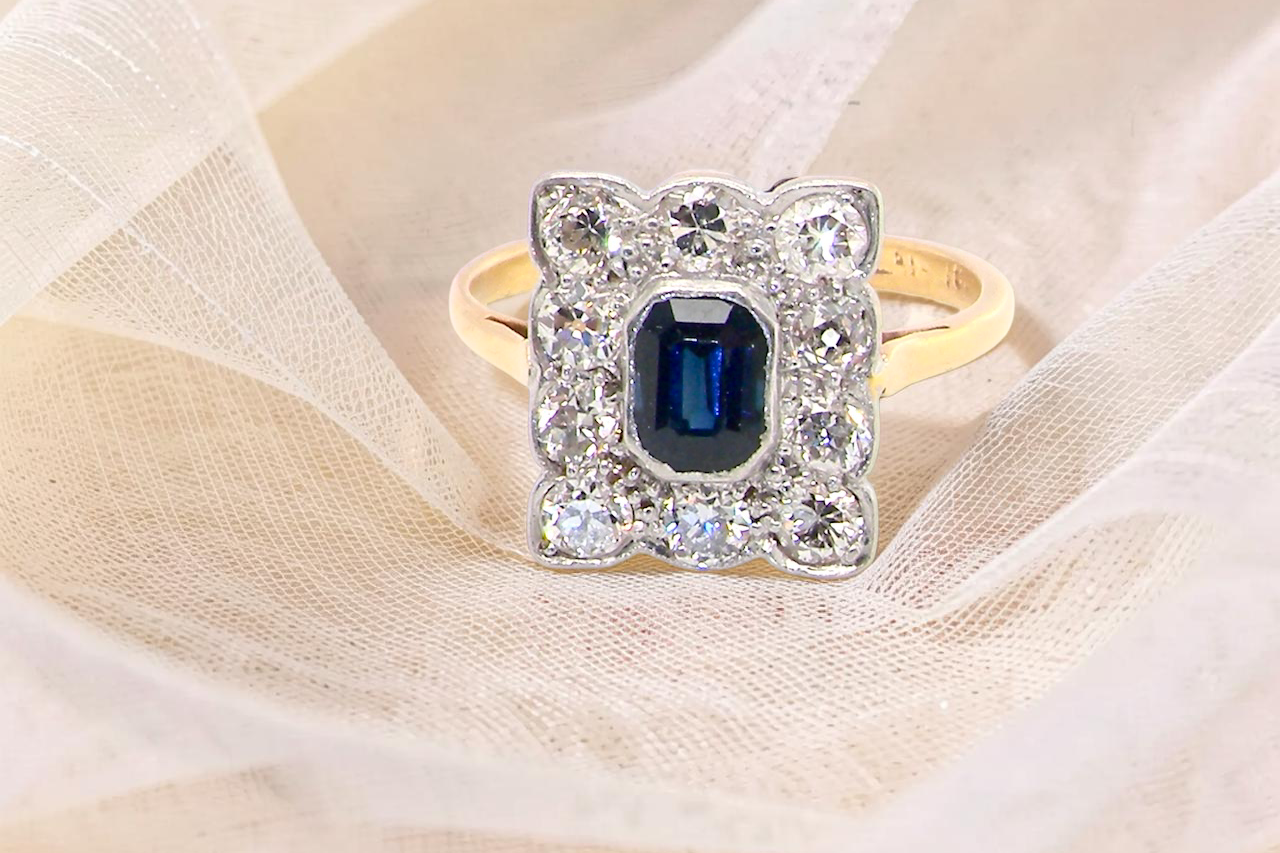 A rectangular cluster ring that features in its centre a cushion shaped dark blue sapphire, that measures (est 0.30 carats)