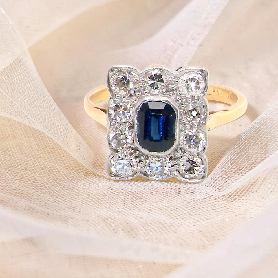 A rectangular cluster ring that features in its centre a cushion shaped dark blue sapphire, that measures (est 0.30 carats)