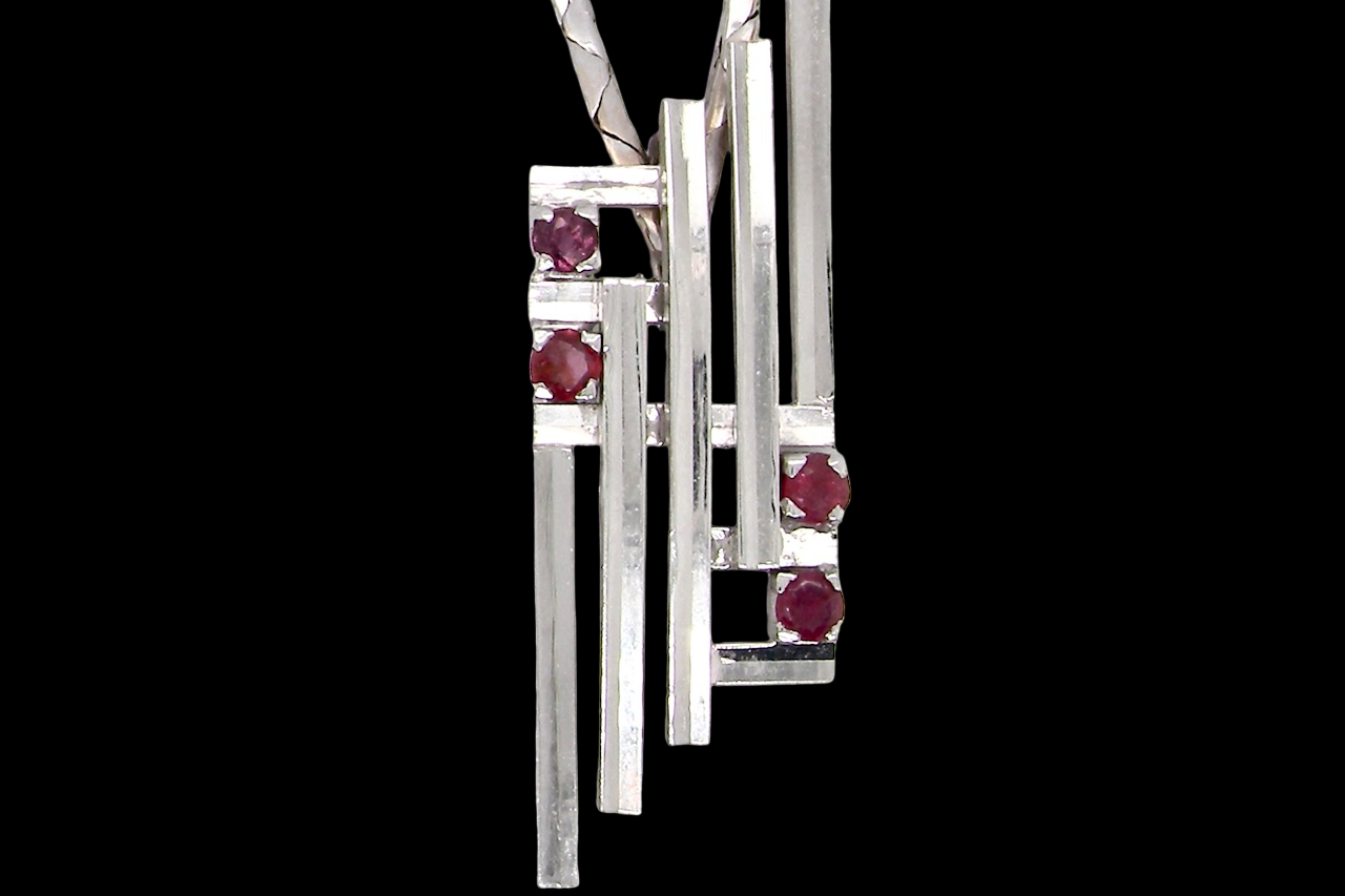 A striking modern pendant set with four 3mm rubies. The pendant measures approximately 40mm x 14mm and features a design of five horizontal bars, with the outer bars each set with vibrant round rubies.