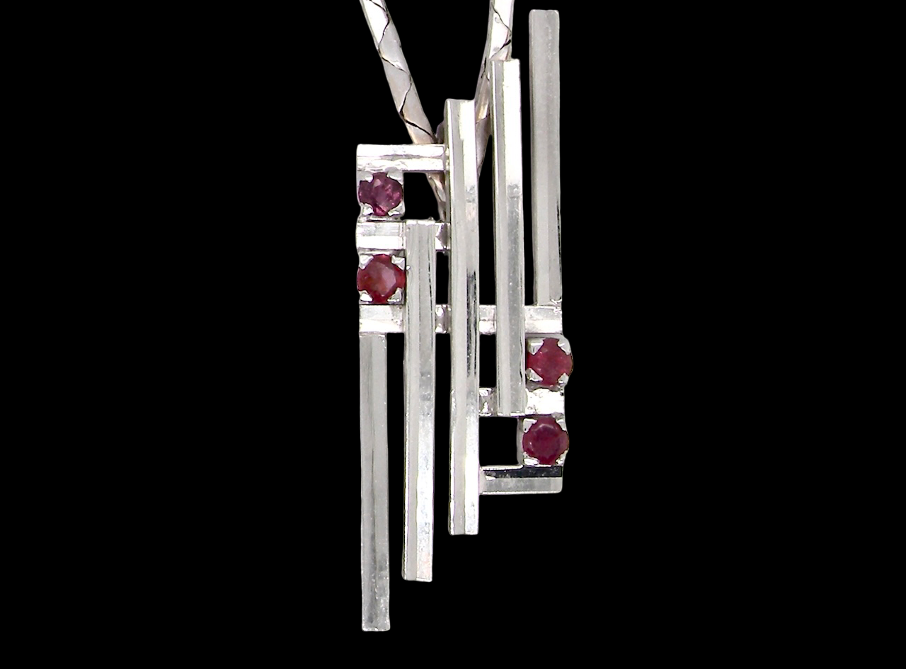 A striking modern pendant set with four 3mm rubies. The pendant measures approximately 40mm x 14mm and features a design of five horizontal bars, with the outer bars each set with vibrant round rubies.