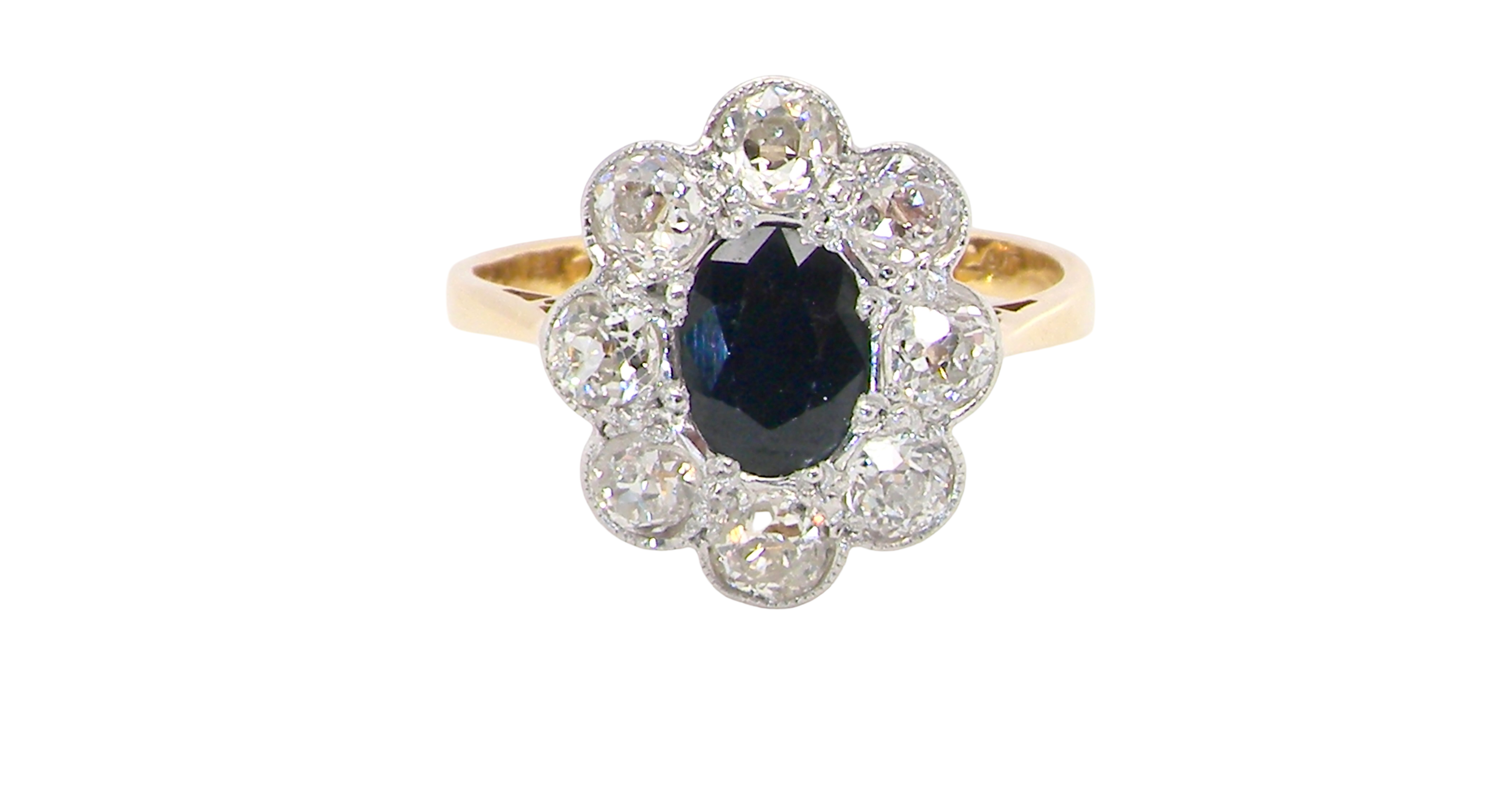 A striking vintage sapphire and diamond cluster ring dating from the 1930s–1940s, beautifully crafted in platinum and 18 carat gold. At the centre sits a richly coloured oval-cut sapphire of deep inky blue-black hue, measuring approximately 7 x 5mm