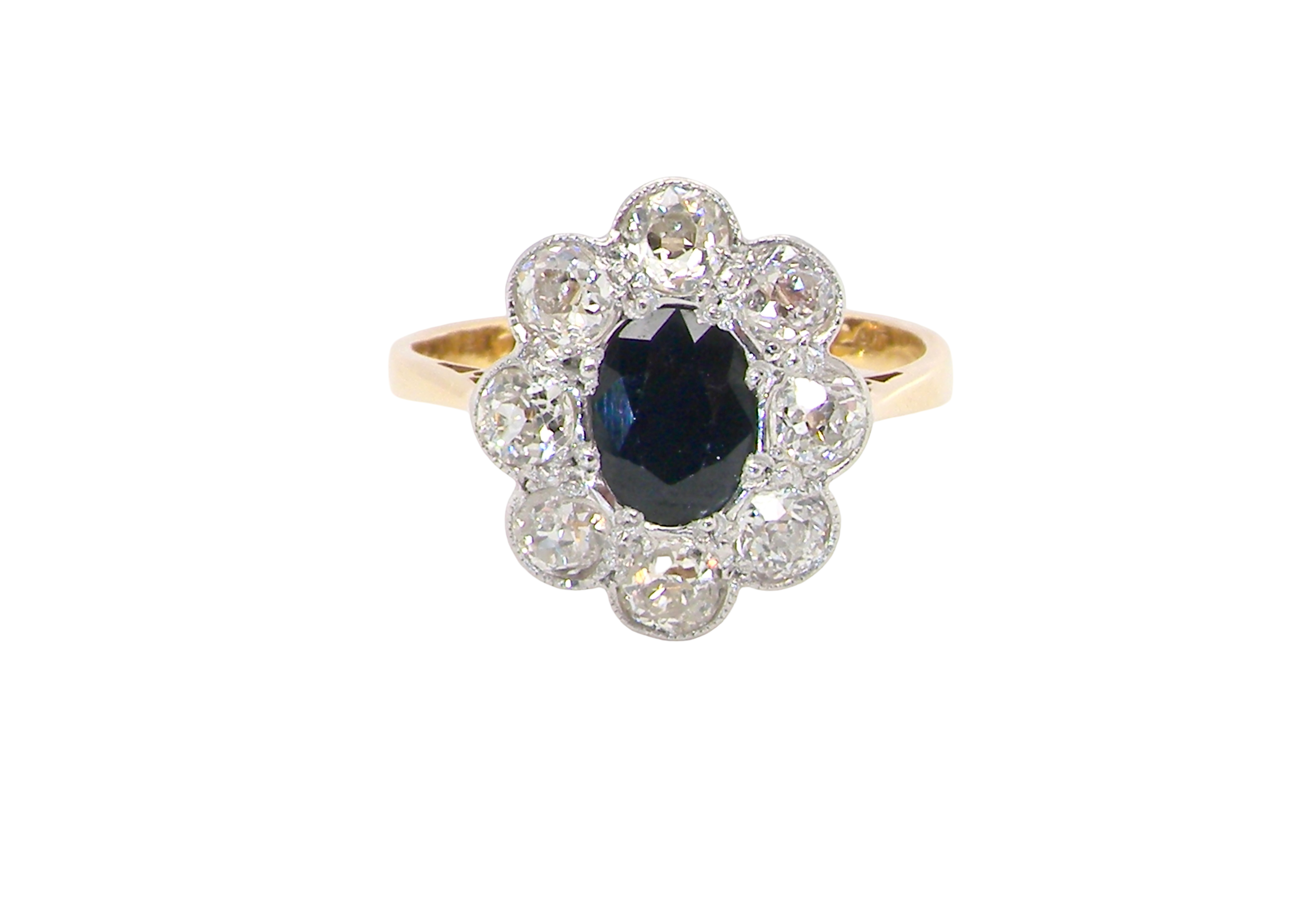 A striking vintage sapphire and diamond cluster ring dating from the 1930s–1940s, beautifully crafted in platinum and 18 carat gold. At the centre sits a richly coloured oval-cut sapphire of deep inky blue-black hue, measuring approximately 7 x 5mm