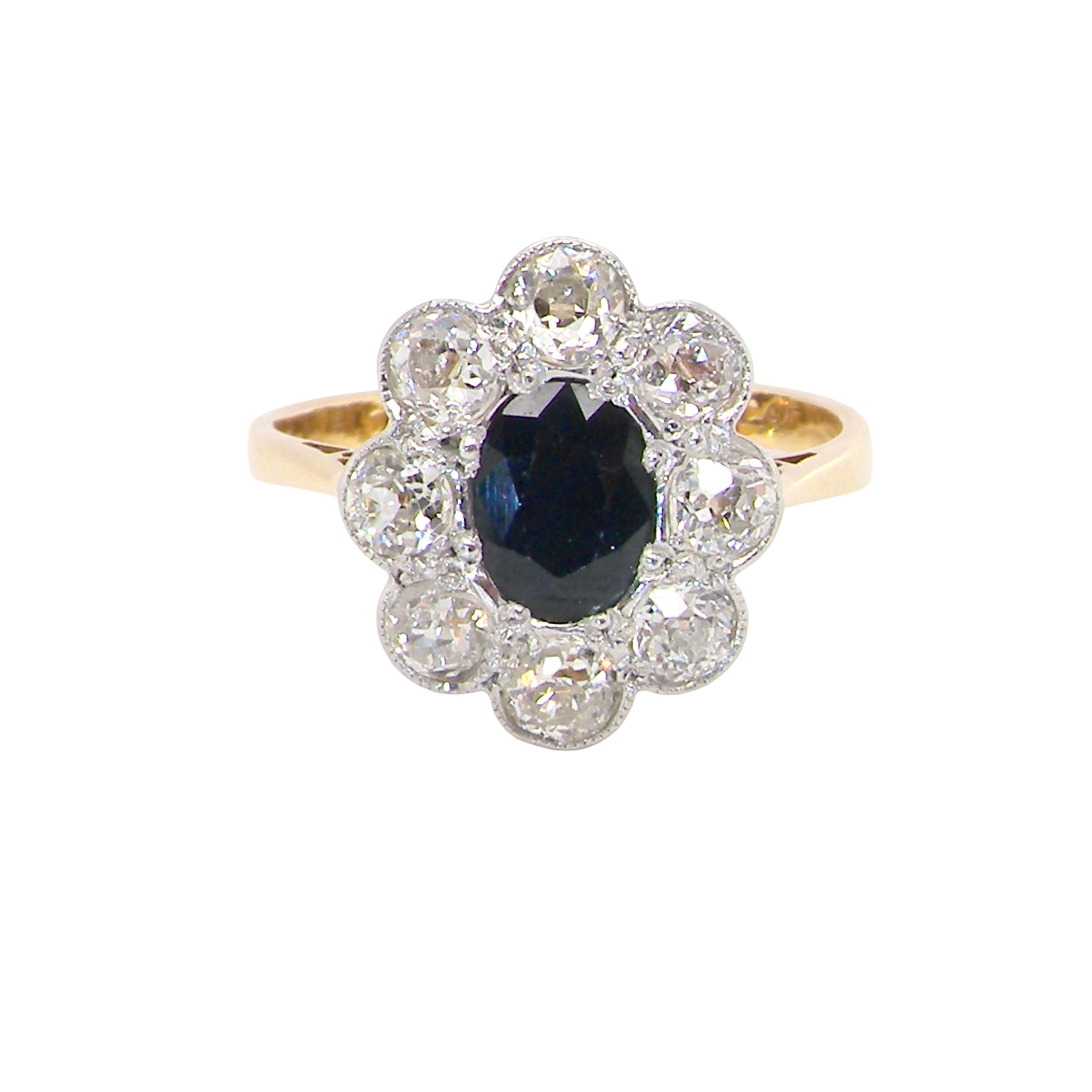 A striking vintage sapphire and diamond cluster ring dating from the 1930s–1940s, beautifully crafted in platinum and 18 carat gold. At the centre sits a richly coloured oval-cut sapphire of deep inky blue-black hue, measuring approximately 7 x 5mm