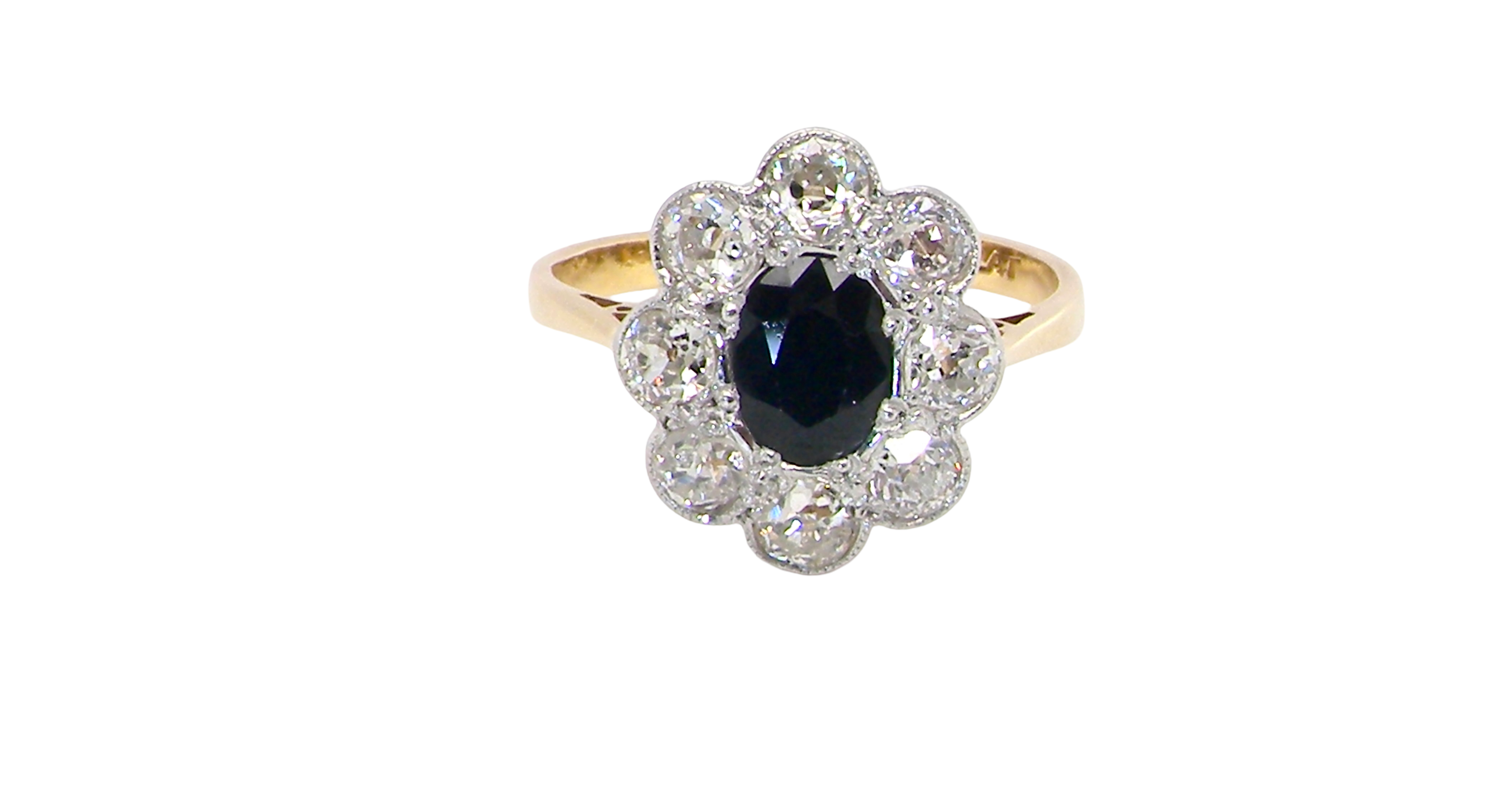 A striking vintage sapphire and diamond cluster ring dating from the 1930s–1940s, beautifully crafted in platinum and 18 carat gold. At the centre sits a richly coloured oval-cut sapphire of deep inky blue-black hue, measuring approximately 7 x 5mm and estimated at 0.75 carats.