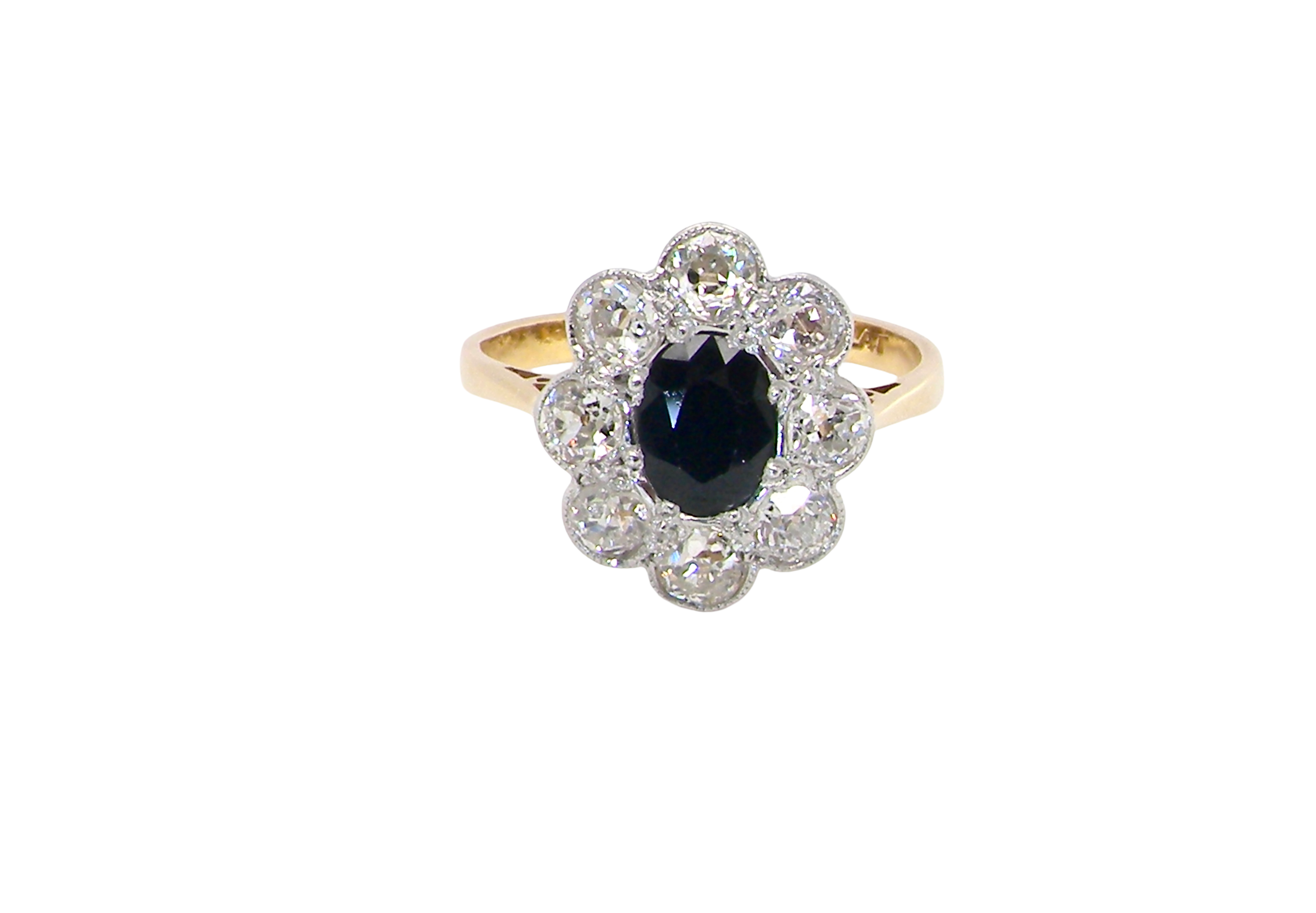 A striking vintage sapphire and diamond cluster ring dating from the 1930s–1940s, beautifully crafted in platinum and 18 carat gold. At the centre sits a richly coloured oval-cut sapphire of deep inky blue-black hue, measuring approximately 7 x 5mm and estimated at 0.75 carats.