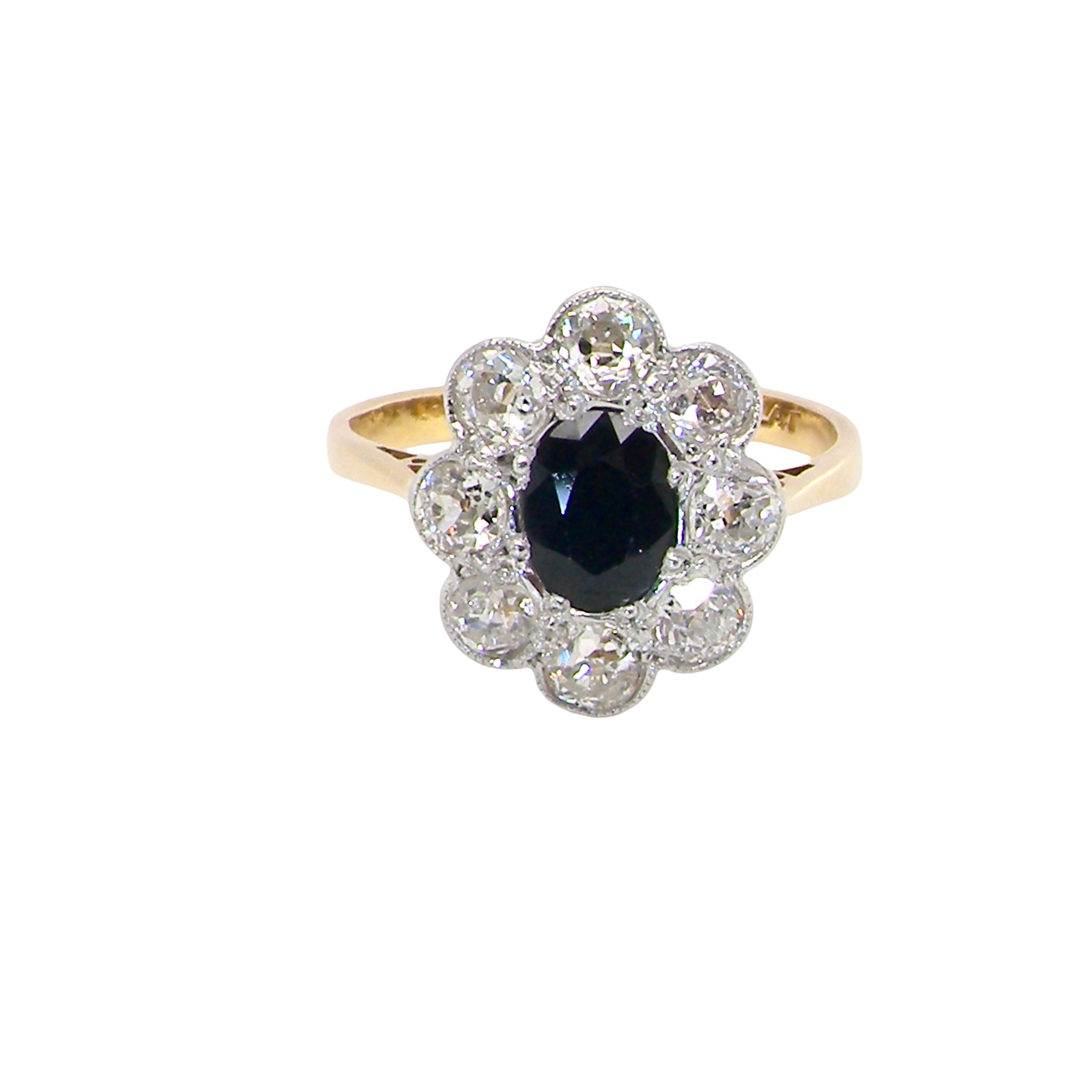 A striking vintage sapphire and diamond cluster ring dating from the 1930s–1940s, beautifully crafted in platinum and 18 carat gold. At the centre sits a richly coloured oval-cut sapphire of deep inky blue-black hue, measuring approximately 7 x 5mm and estimated at 0.75 carats.