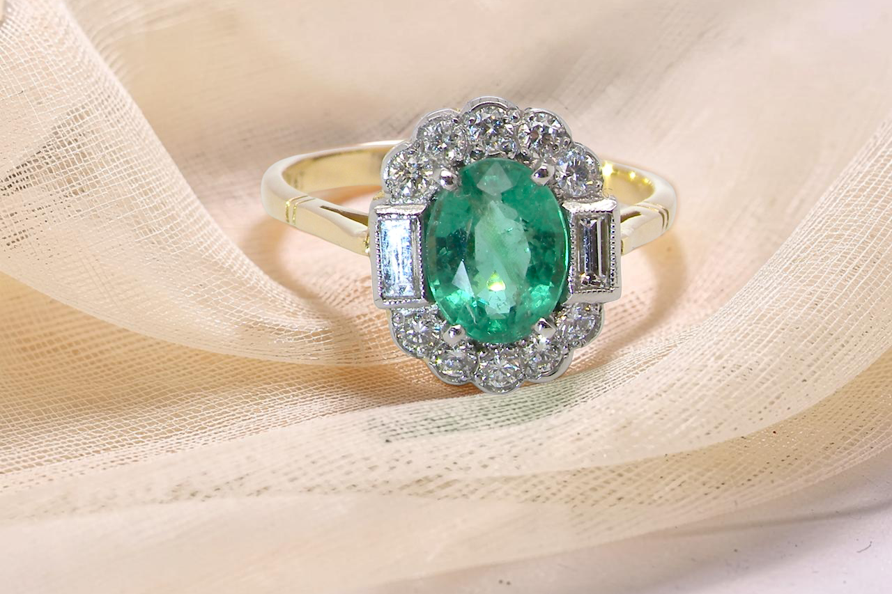 A stunning vintage cluster ring, set with an oval-cut emerald measuring 8 x 6mm, approximately 1.10 carats. The emerald displays a rich, deep grass-green colour with natural inclusions,