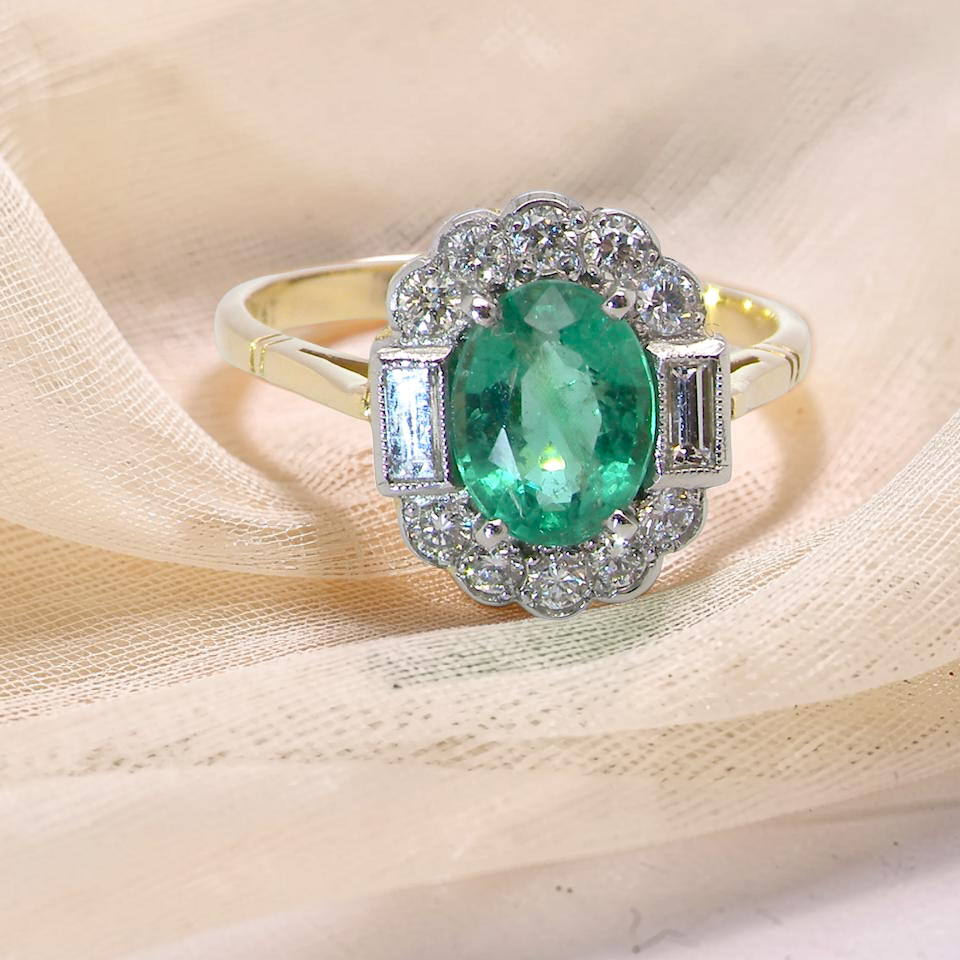 A stunning vintage cluster ring, set with an oval-cut emerald measuring 8 x 6mm, approximately 1.10 carats. The emerald displays a rich, deep grass-green colour with natural inclusions,