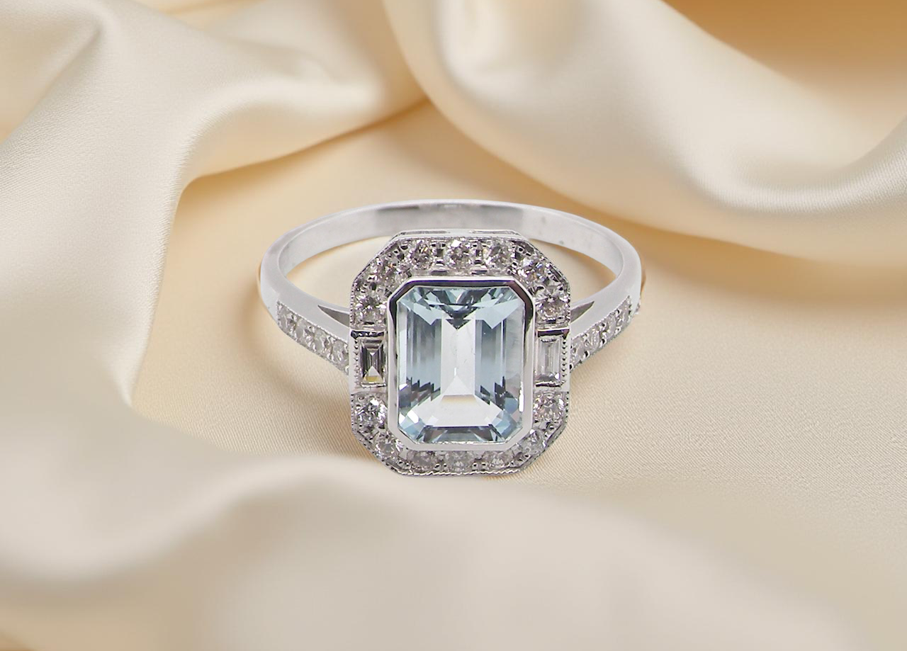 A very pretty cluster ring. Features a step cut aquamarine centre stone, 8x7mm (est 1.21 carats). Plain rim setting. A