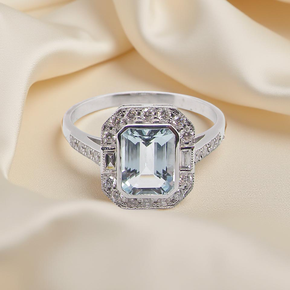 A very pretty cluster ring. Features a step cut aquamarine centre stone, 8x7mm (est 1.21 carats). Plain rim setting. A