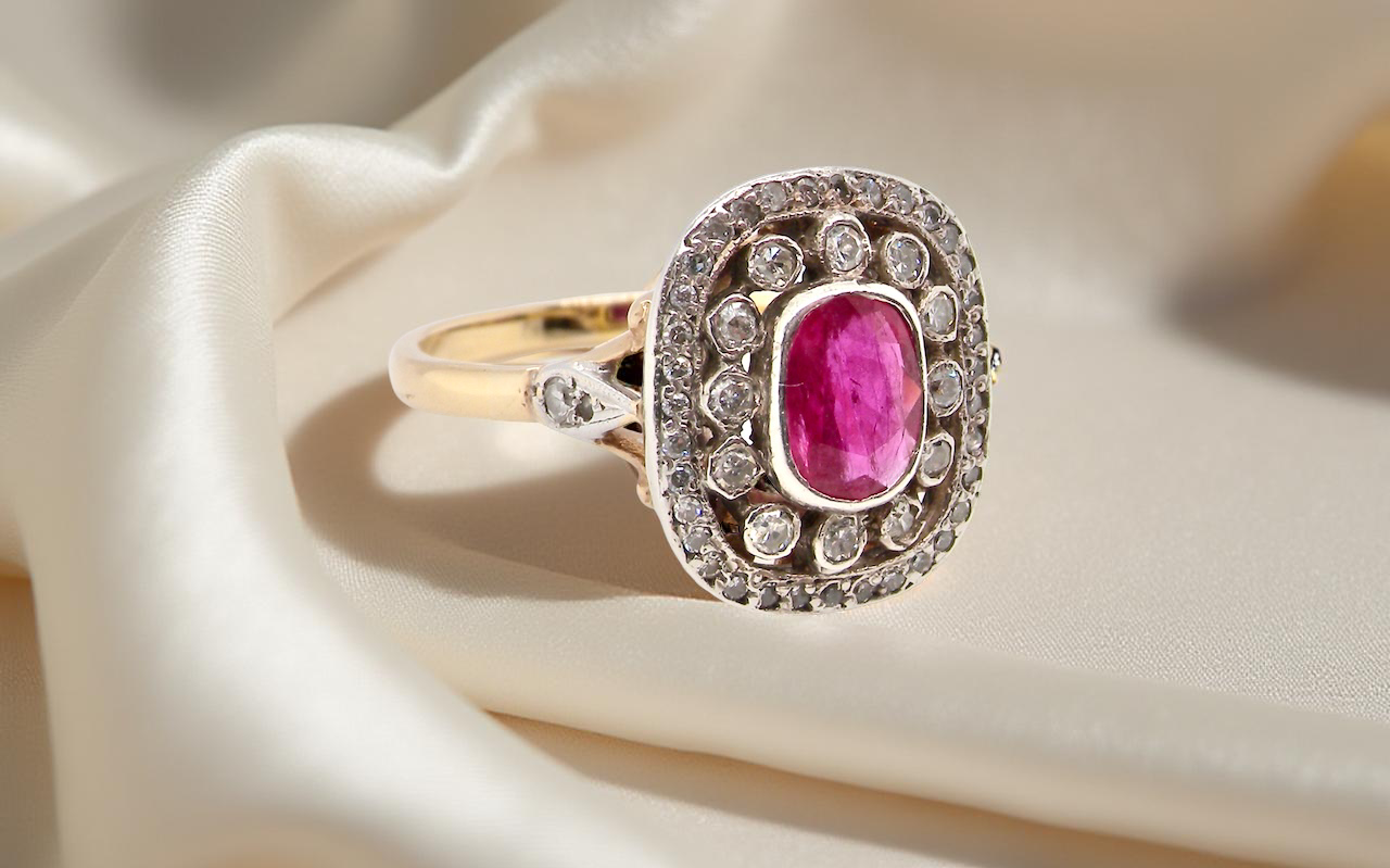 Gold ring with a pink gemstone and diamond accents on beige fabric