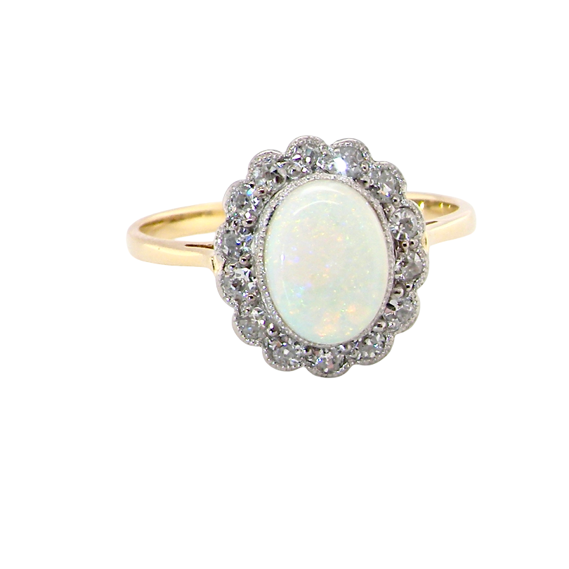 A yellow gold ring featuring a central oval white opal surrounded by a halo of small clear stones, set against a plain white background.