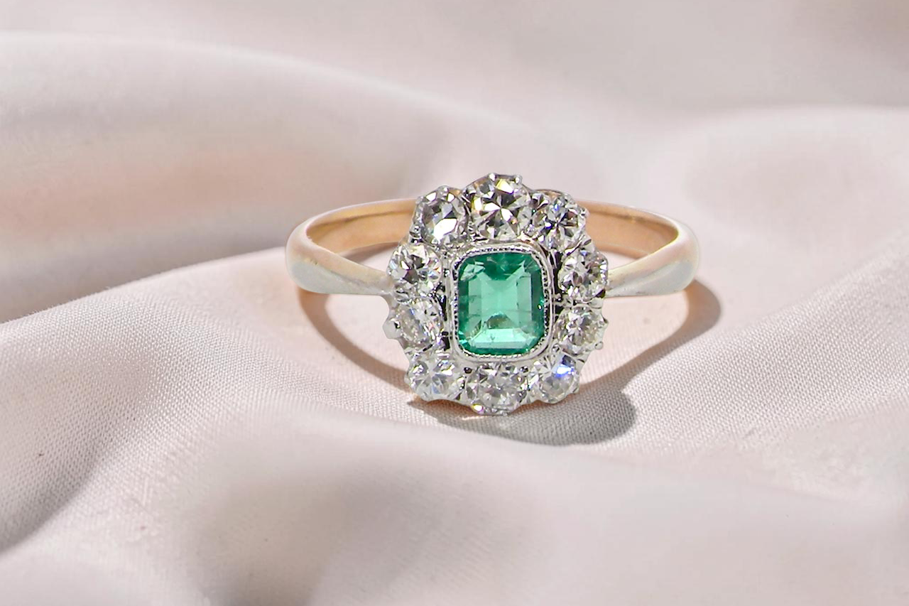 cluster ring, the centre stone a cushion shaped emerald 4x3.5mm, mid to dark green colour. Mille grain setting.