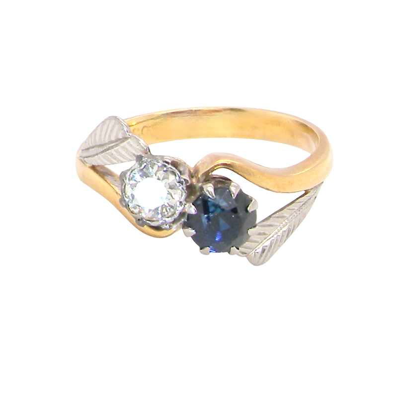 A two-tone ring featuring a yellow gold band, a silver-toned leaf-shaped setting, a clear round-cut gemstone, and a dark blue oval-cut gemstone, shown on a plain white background.