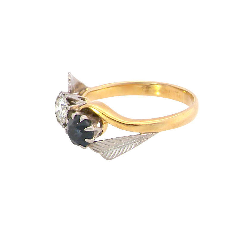 A vintage-style gold ring with a curved yellow gold band, a clear round gemstone, and a central black oval gemstone surrounded by textured silver-toned leaf-like settings, shown on a plain white background.