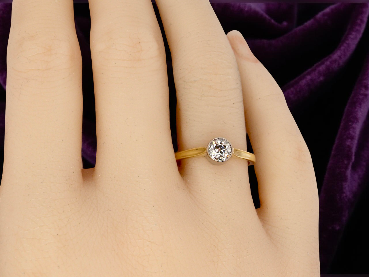 Gold ring with a diamond on a hand against a purple fabric background