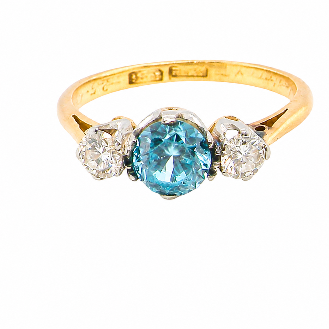 A vintage three stone ring. Centre stone, a round 5.8mm natural blue zircon.
To each side an old brilliant cut white diamond 4mm round (est 0.25 carats).
