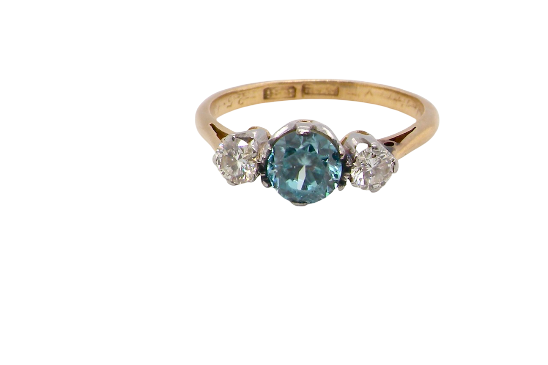 A vintage three stone ring. Centre stone, a round 5.8mm natural blue zircon.
To each side an old brilliant cut white diamond 4mm round (est 0.25 carats). Colour i-j, clarity Si.
