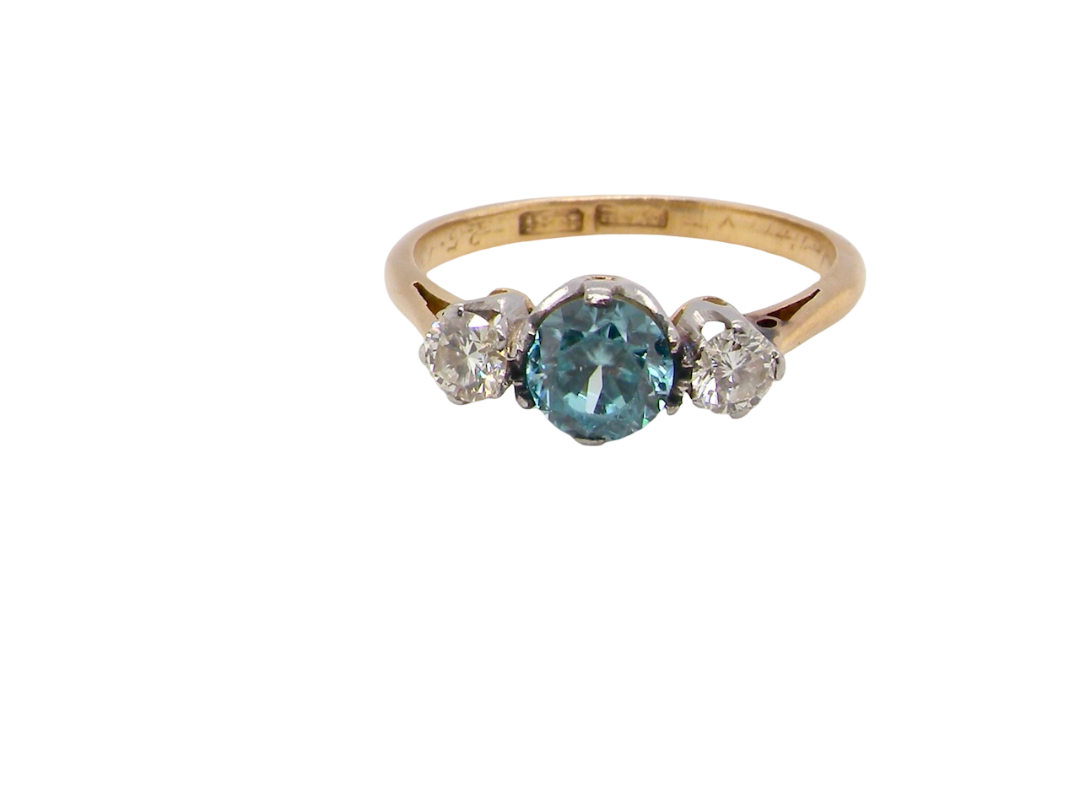 A vintage three stone ring. Centre stone, a round 5.8mm natural blue zircon.
To each side an old brilliant cut white diamond 4mm round (est 0.25 carats). Colour i-j, clarity Si.
