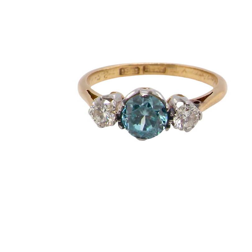 A vintage three stone ring. Centre stone, a round 5.8mm natural blue zircon.
To each side an old brilliant cut white diamond 4mm round (est 0.25 carats). Colour i-j, clarity Si.
