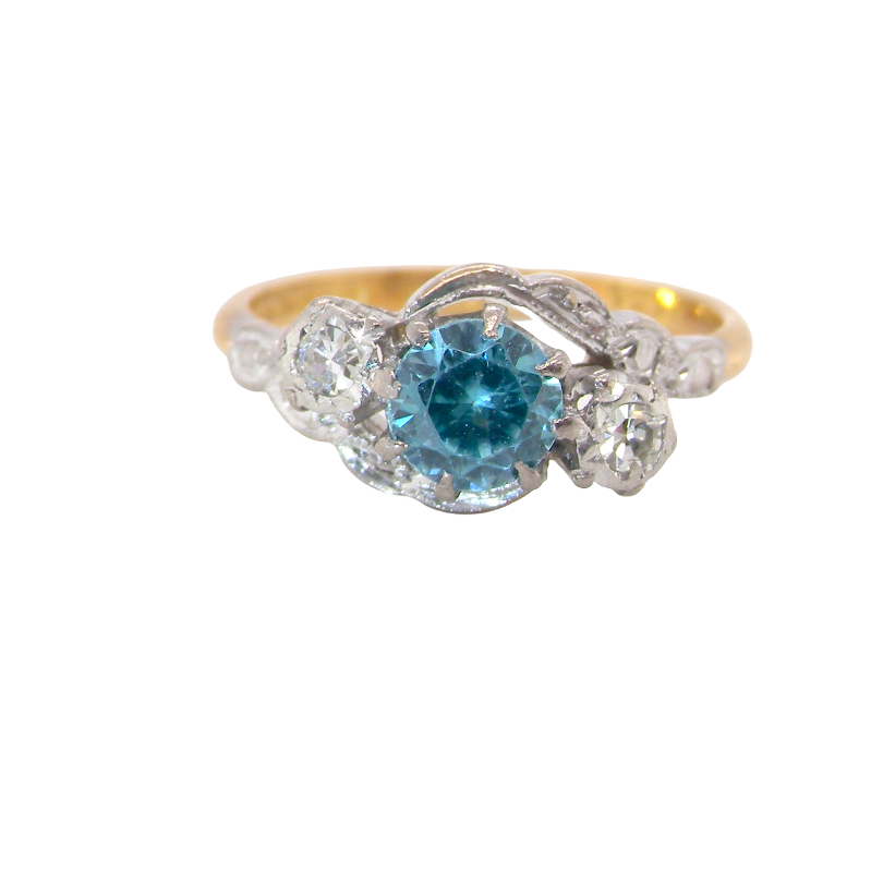 A vintage three stone ring, cross over style and features a round 6mm blue zircon centre stone