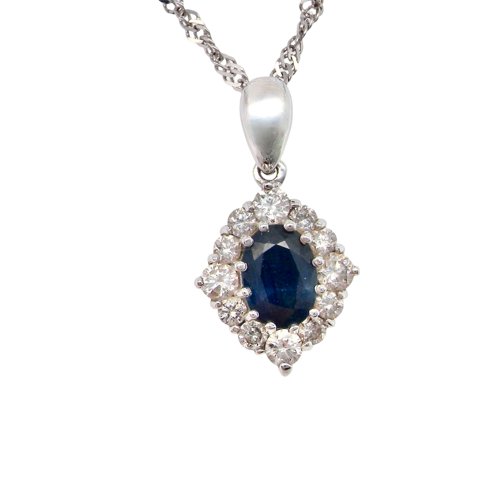 A white gold pendant. The centre stone an inky black blue sapphire 7x5mm, claw set. Complimented by an outer halo of brilliant cut white diamonds.