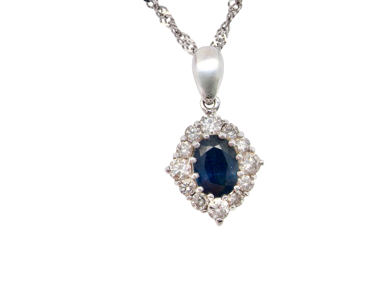 A white gold pendant. The centre stone an inky black blue sapphire 7x5mm, claw set. Complimented by an outer halo of brilliant cut white diamonds.
