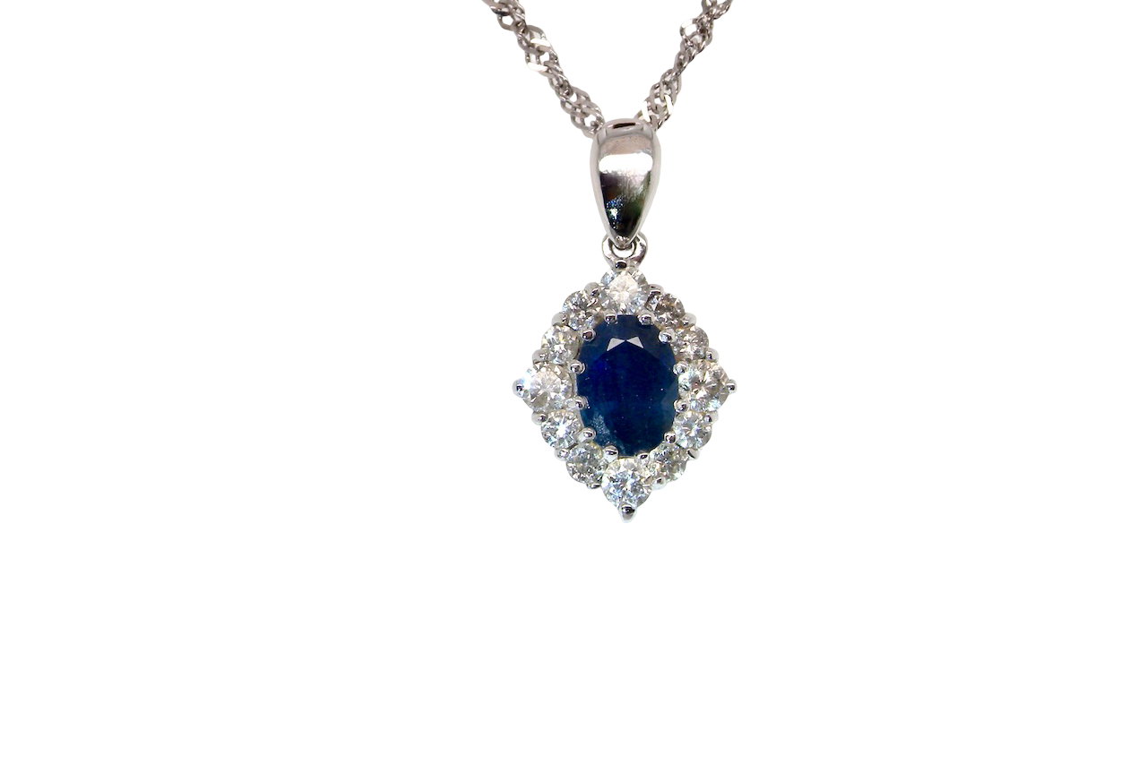 A white gold pendant. The centre stone an inky black blue sapphire 7x5mm, claw set. Complimented by an outer halo of twelve brilliant cut white diamonds.